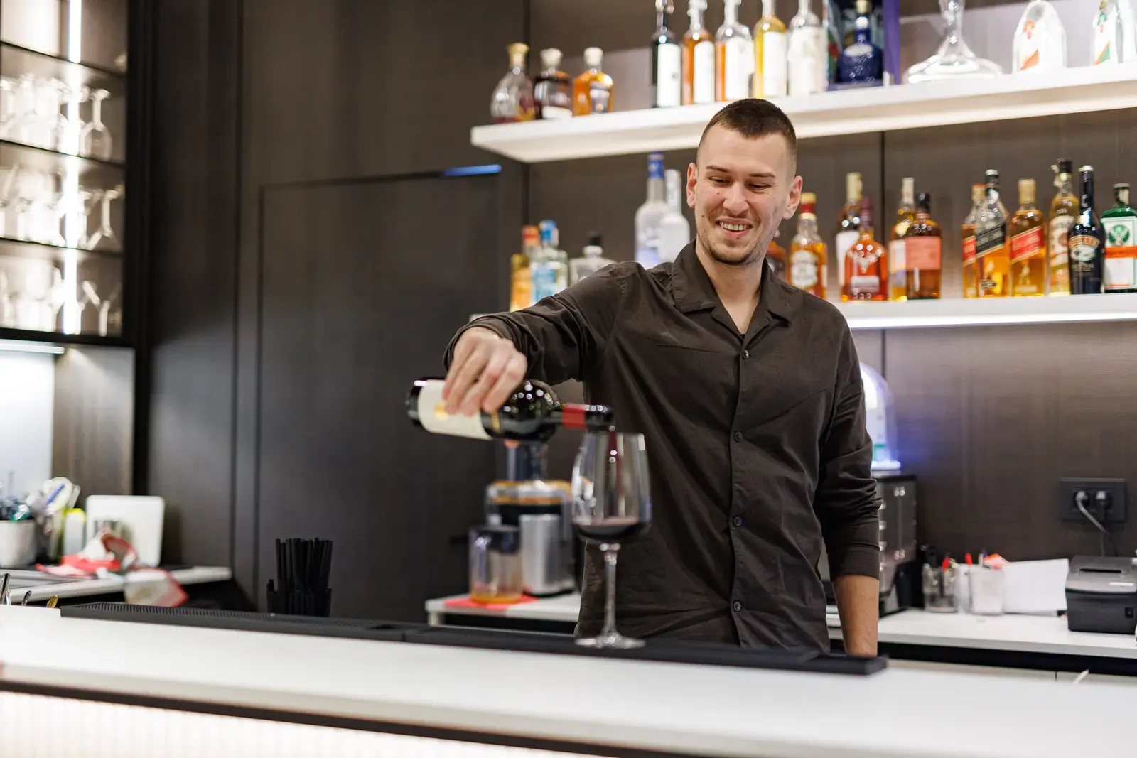 Barmen u Force House-u sipa crno vino ispred police sa pićem